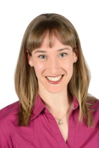 Sara wearing a pink collared shirt with shoulder-length brown blonde hair and smiling at the camera.
